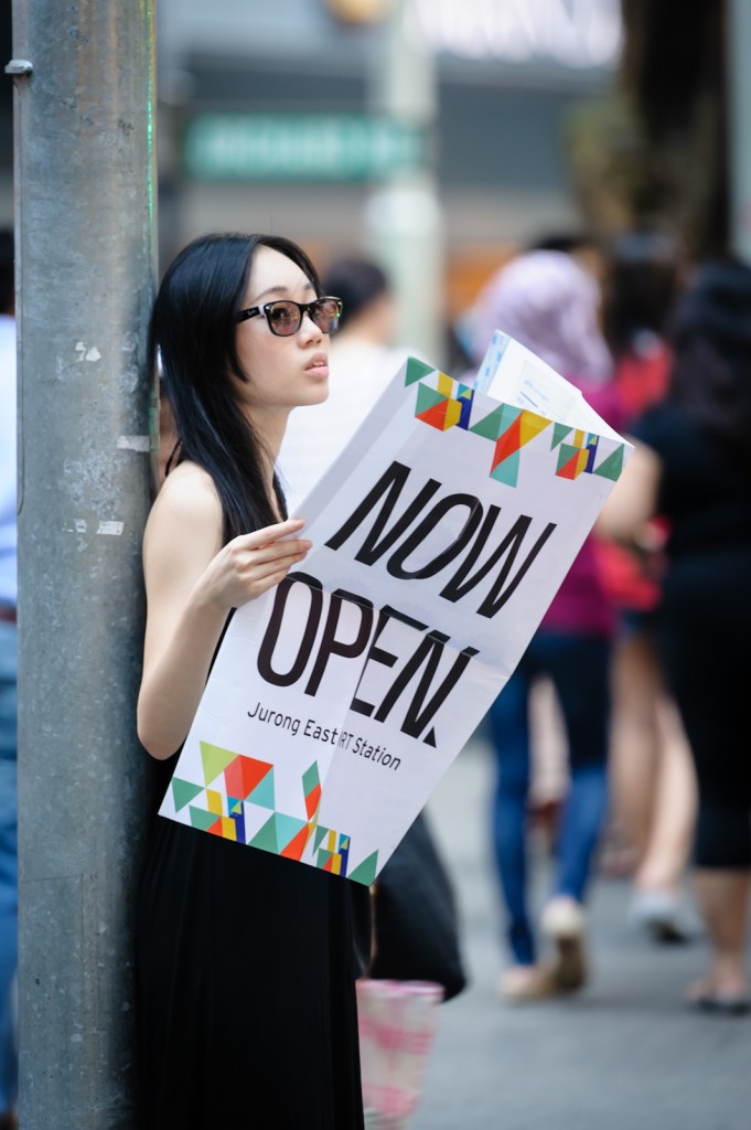 Street photography - Girl holding newspaper that says "Now Open"