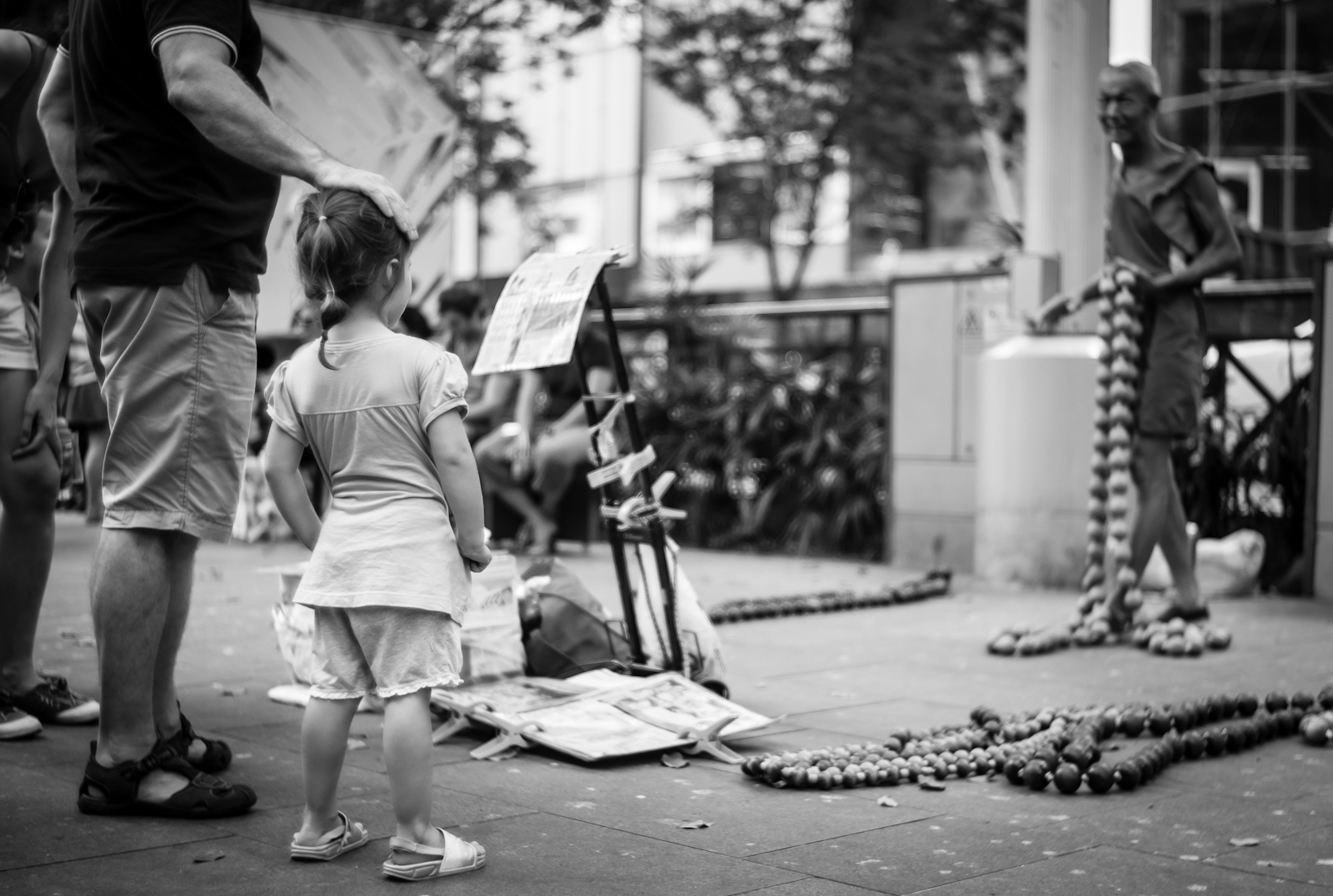 Street photography - Man patting his daughter's head as she watches the street performer
